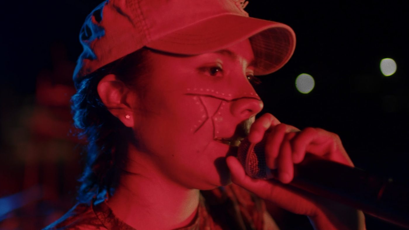 Celika canta ante el micrófono bajo luces rojas